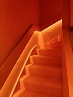 Orange-lit staircase with glowing handrail and orange walls.