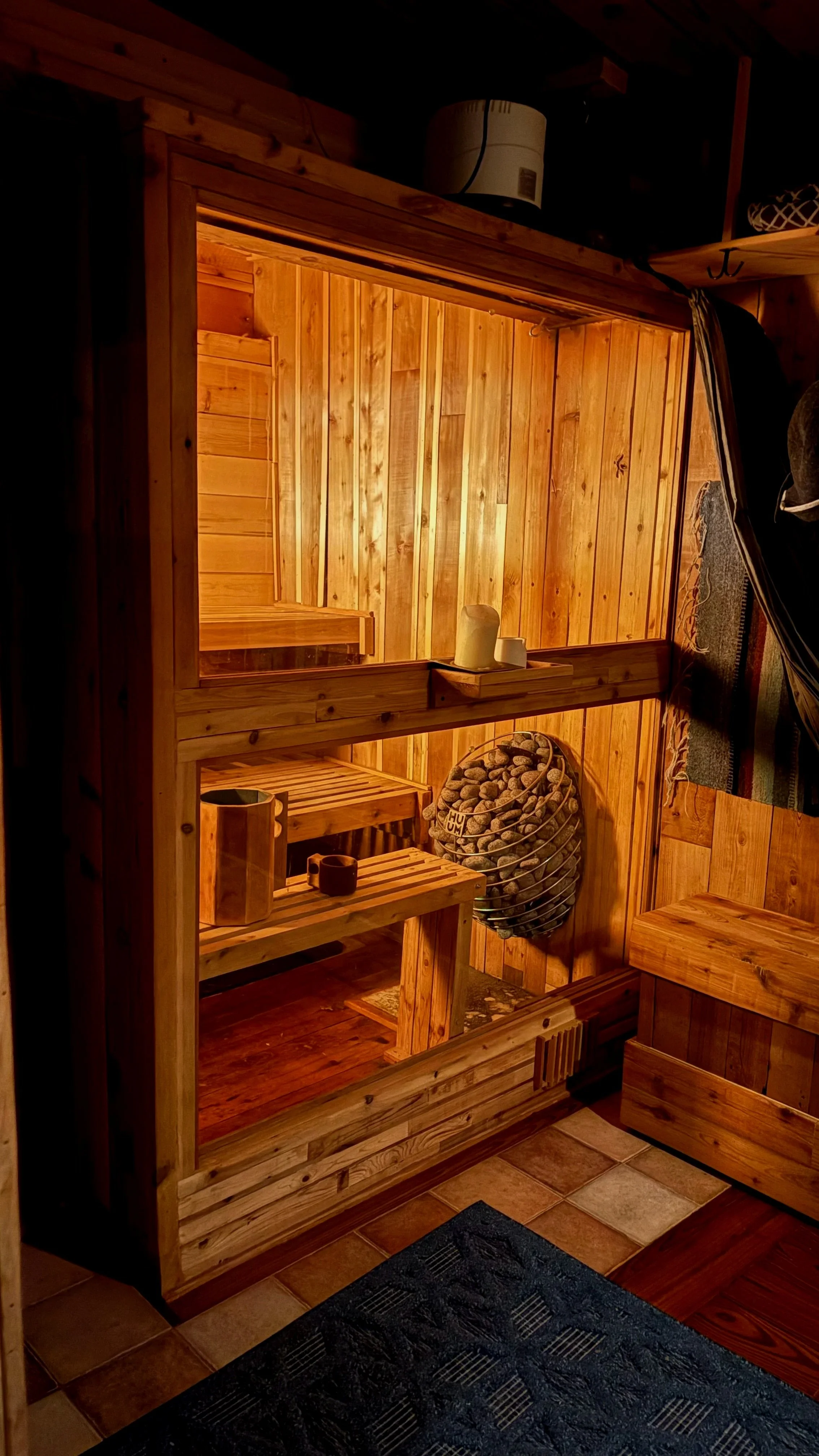 Wood-paneled sauna room with benches, a heater, candles, and a bucket of sauna stones.