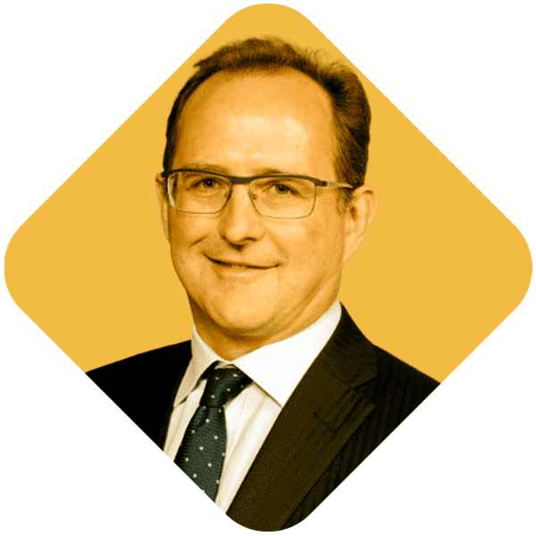 A man in a suit with glasses, smiling against a yellow background.