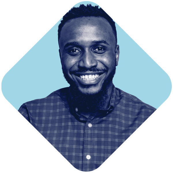 A man smiling with a beard and short hair, wearing a checkered shirt, against a blue background.