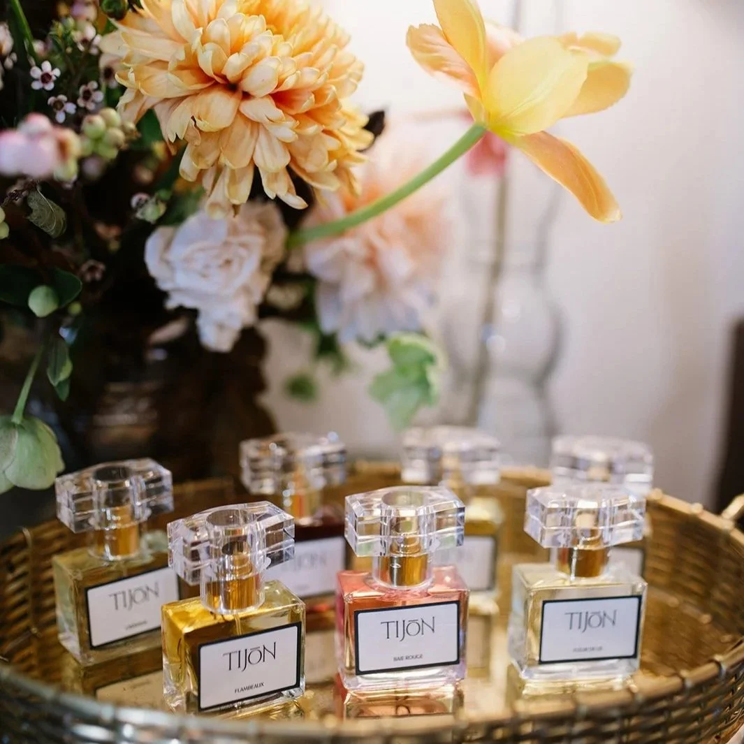 A basket containing small bottles of perfume named Tijon, surrounded by a floral arrangement with peach, pink, and white flowers.