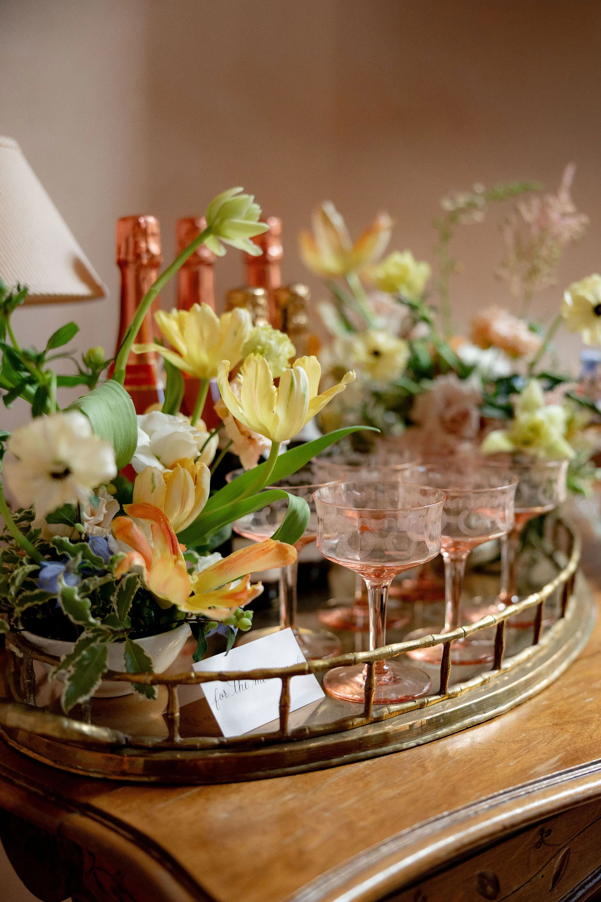 A decorative tray with fresh flowers and pink glassware on a wooden surface.