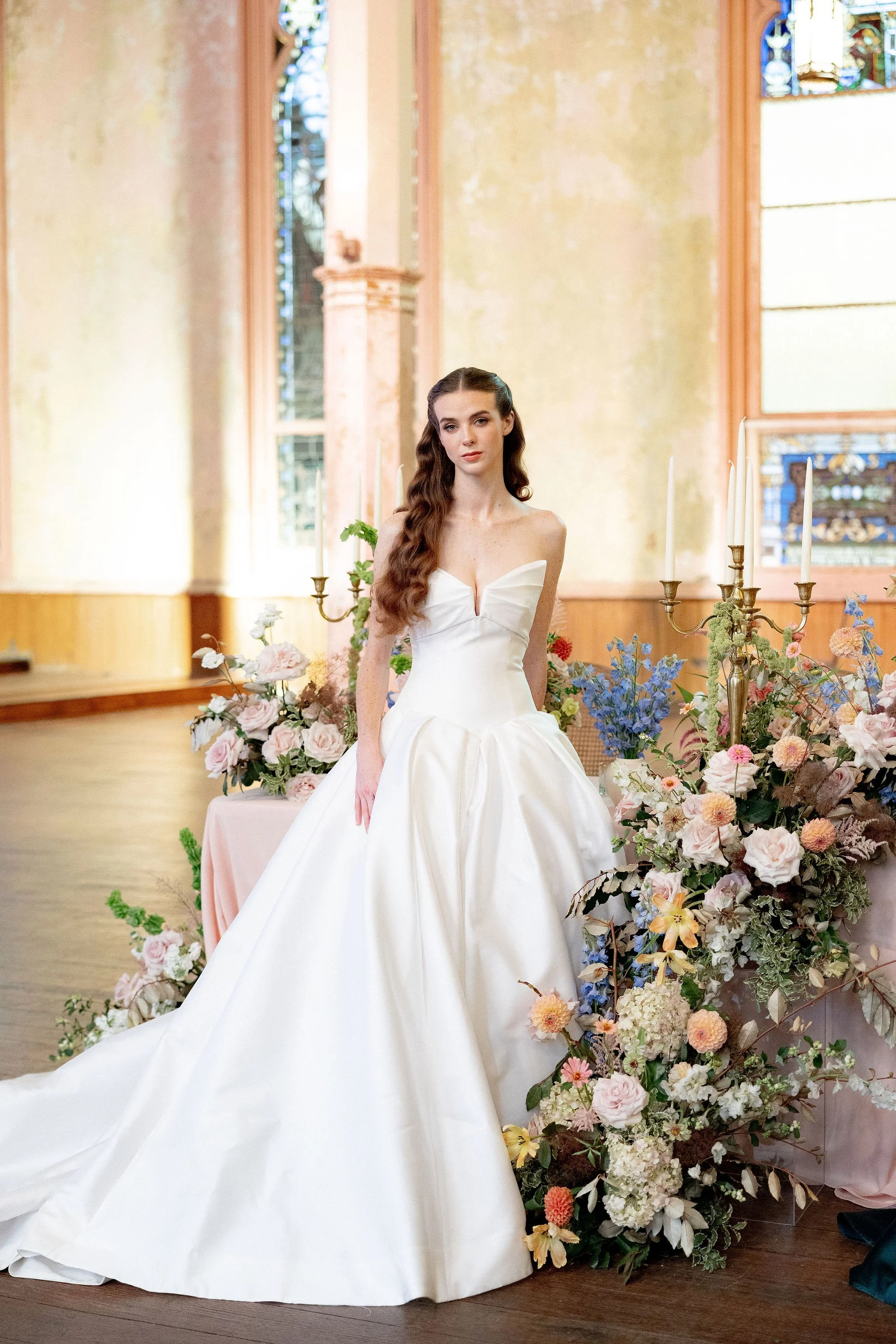 A woman in a strapless wedding gown standing in a decorated venue with flowers and candelabras.