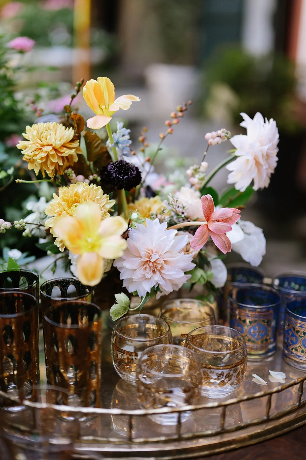 A floral arrangement in a vase with various flowers, surrounded by ornate glass candle holders on a tray.