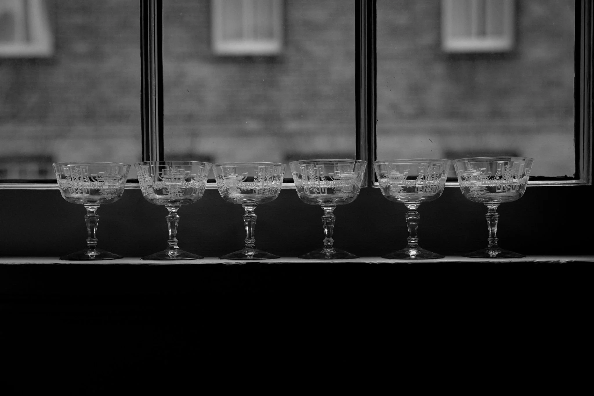Six glass bowls with etched designs on a windowsill, with a blurred building visible outside the window.