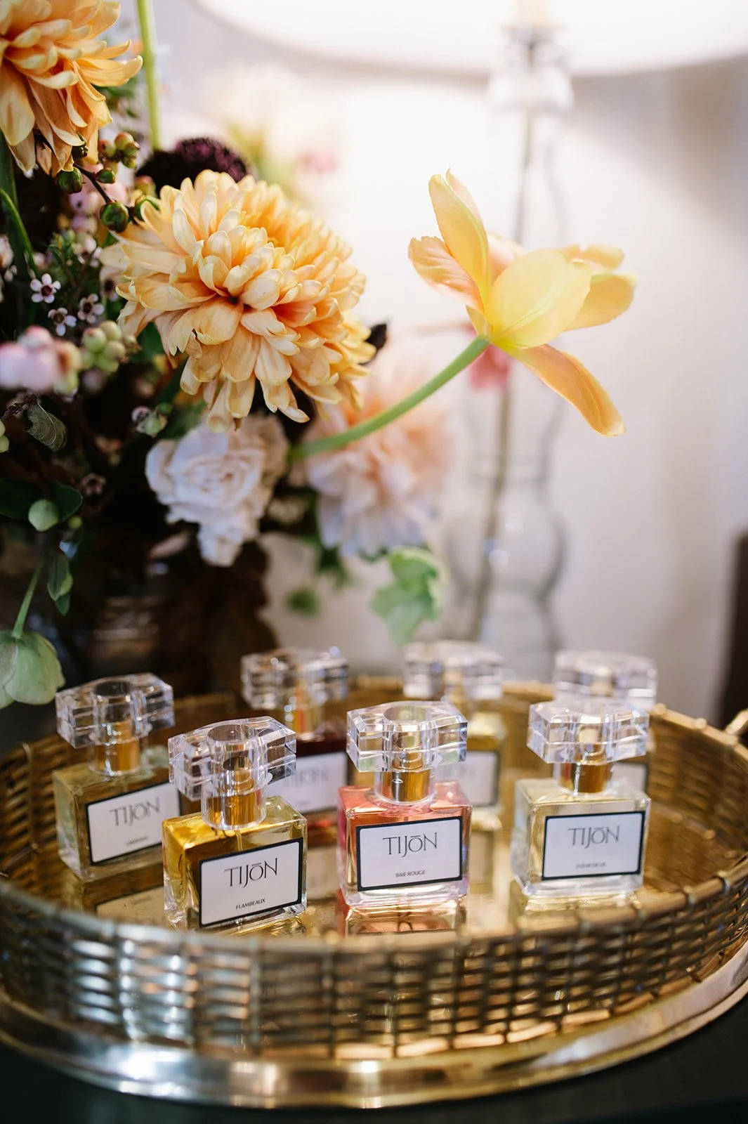 Display of perfume bottles in a gold tray with a floral arrangement including yellow and peach flowers in the background.