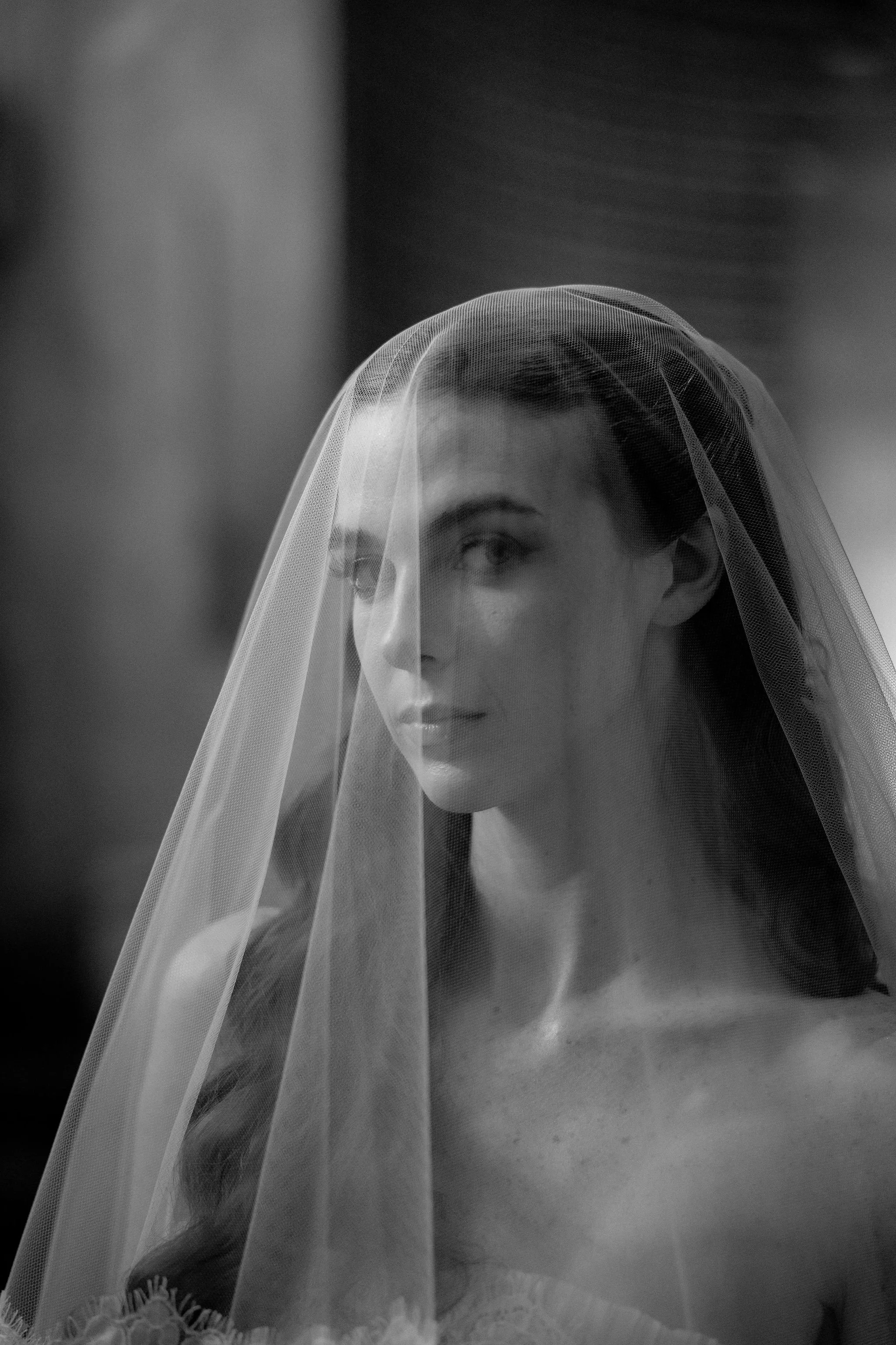 A black and white photograph of a woman with long hair, wearing a wedding veil.