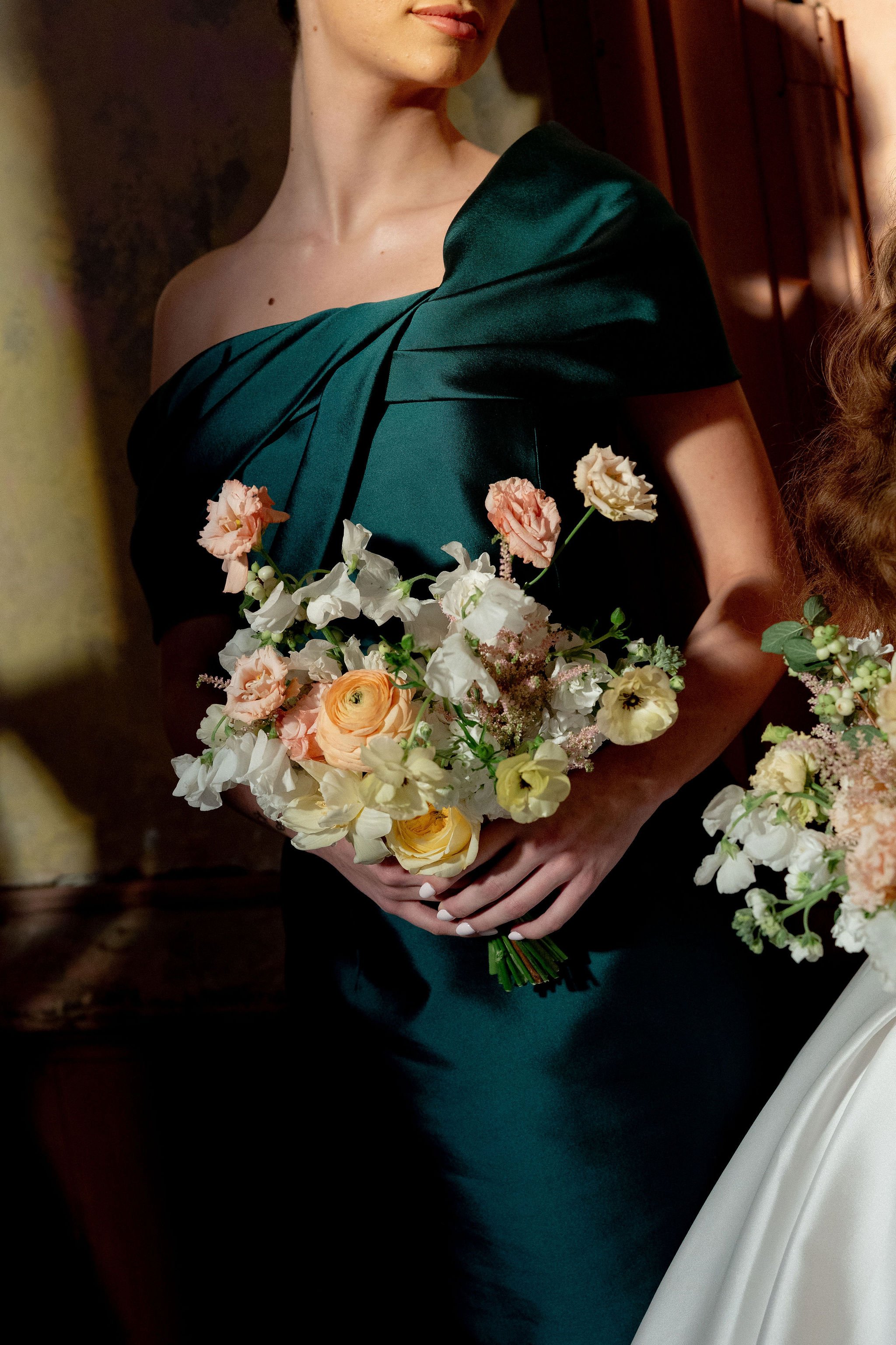A woman in an elegant dark green dress holding a bouquet of flowers.