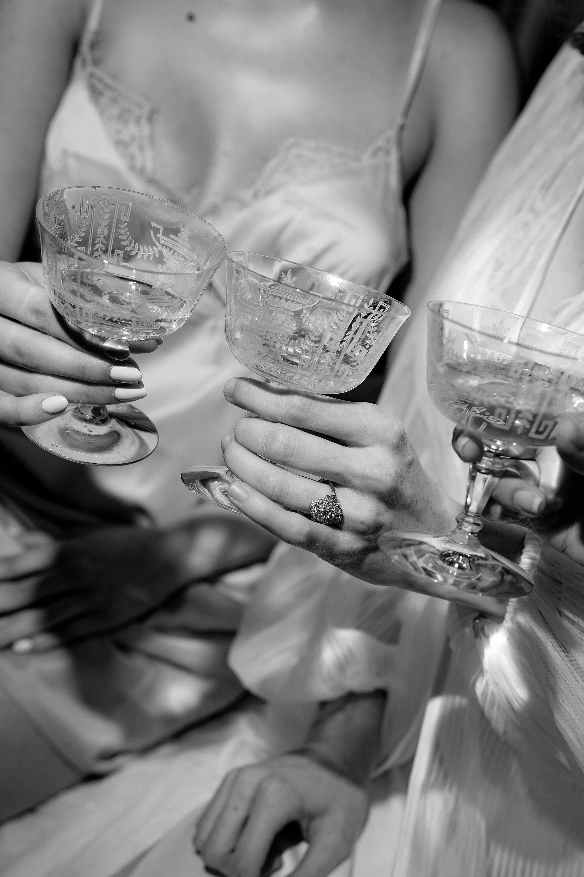 Close-up of three women in cocktail dresses holding crystal champagne glasses in a toast, black and white photograph.