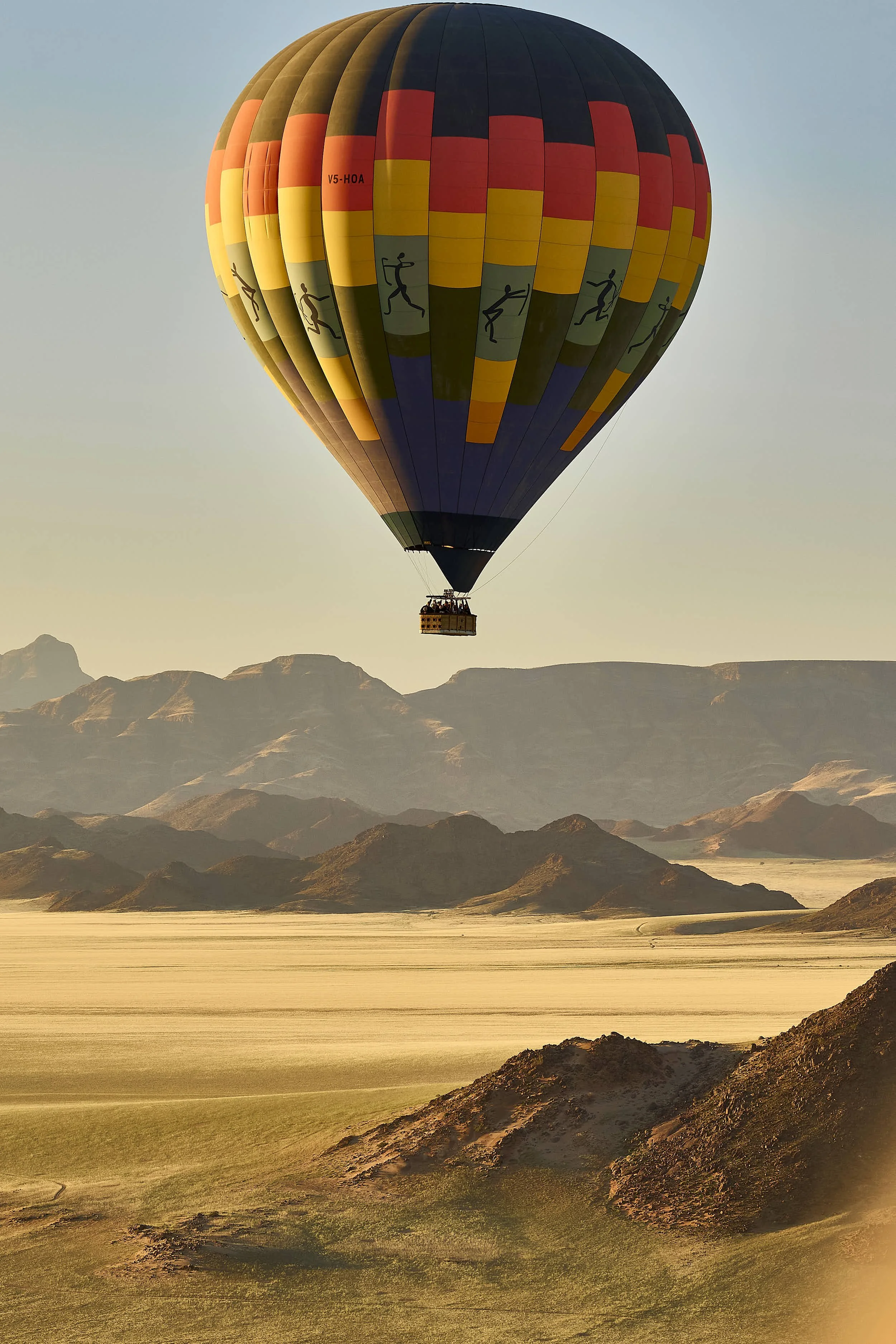 A colorful hot air balloon floating over a desert landscape with mountains in the distance during sunset.