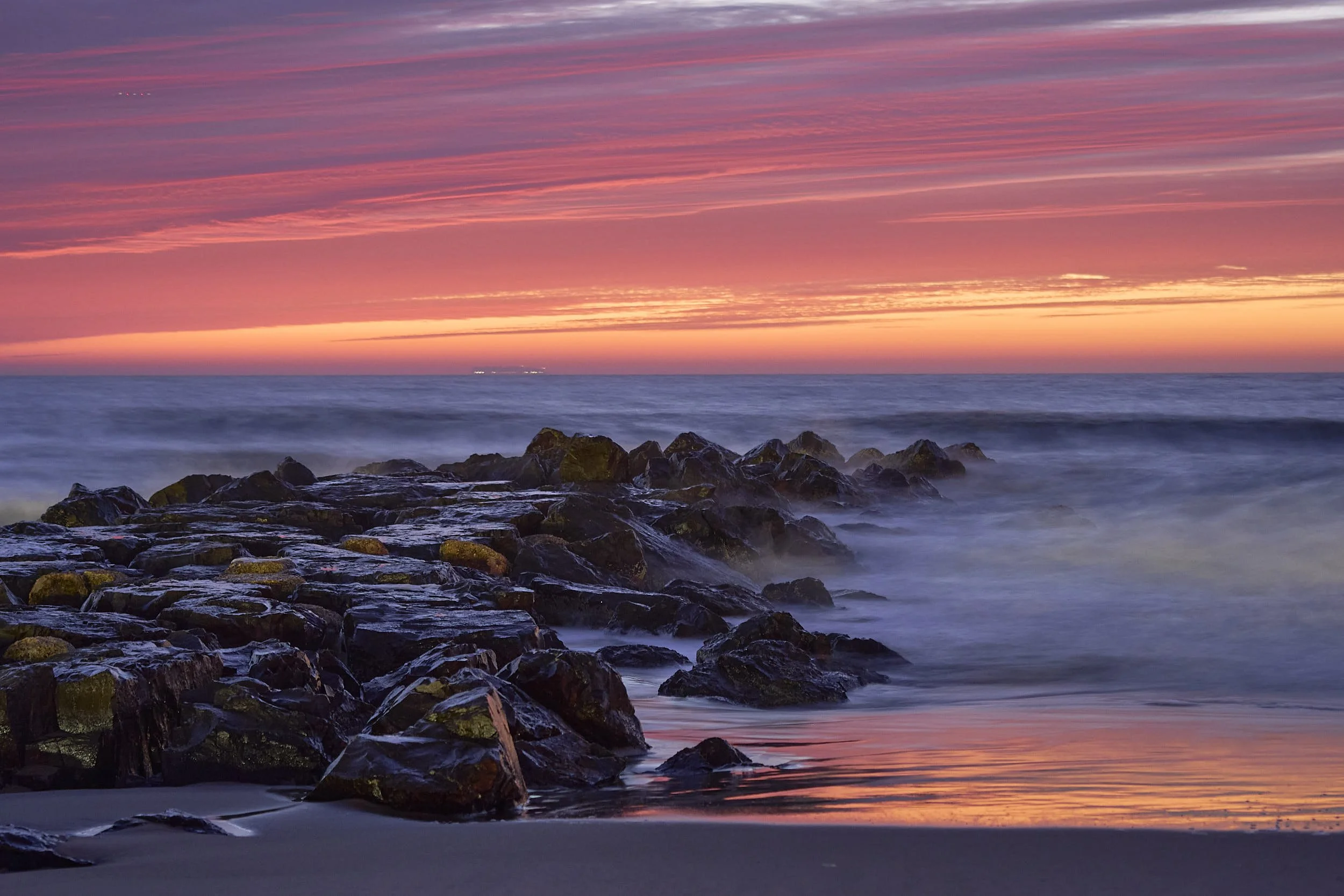 Sunrise at the beach in Asbury Park, nj over the ocean with rocks on the shoreline and colorful sky.