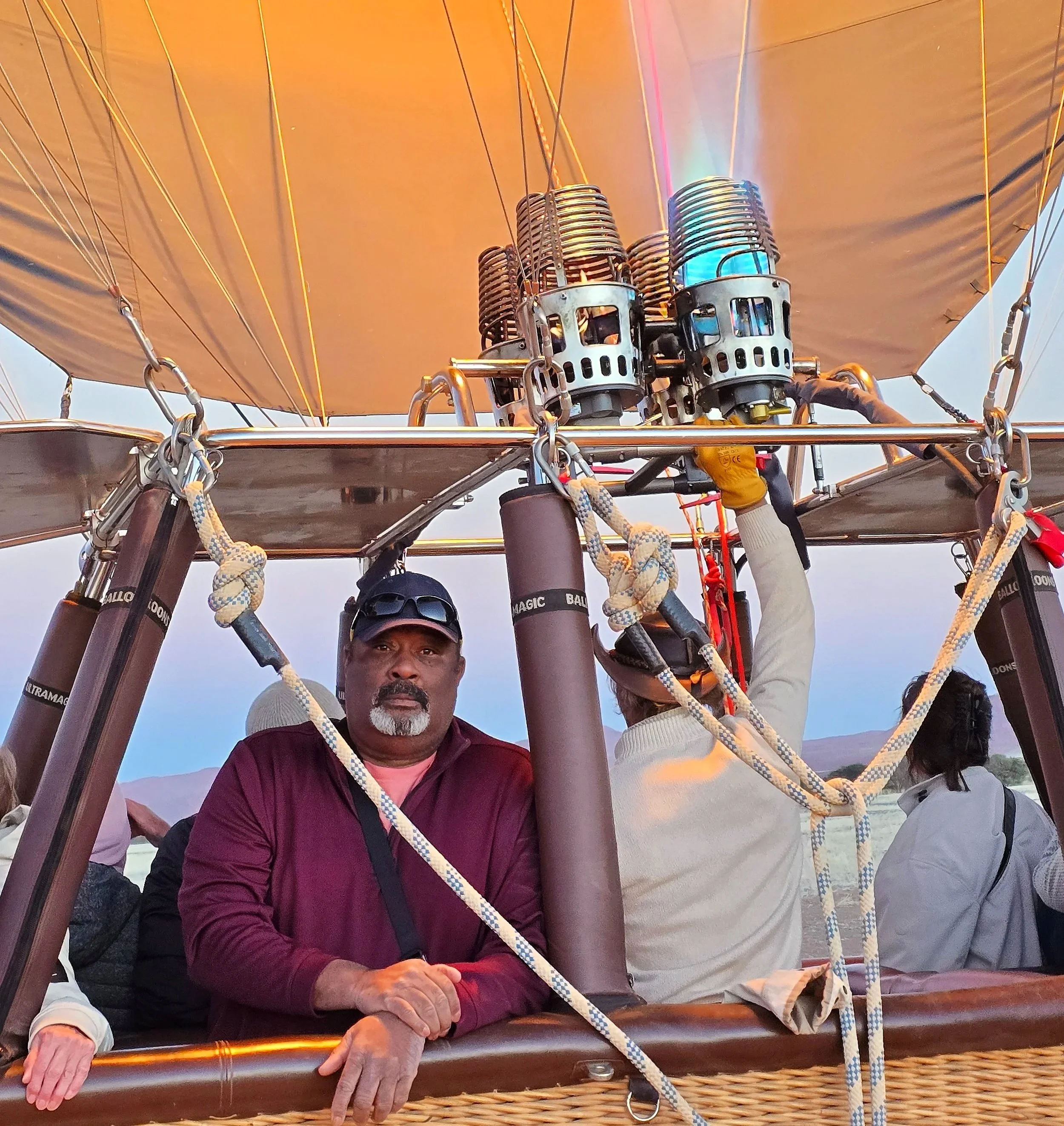 A group of people in a hot air balloon basket, preparing for a flight, with the burner system overhead.