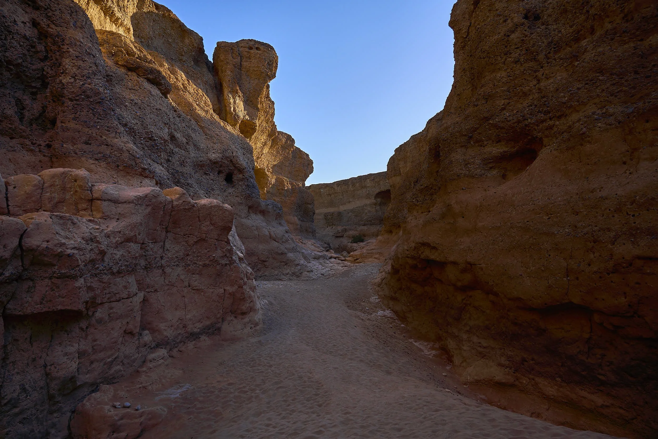A narrow canyon with high reddish-brown rocky walls and sandy ground, under a clear blue sky. Sesriem Canyon, Namibia