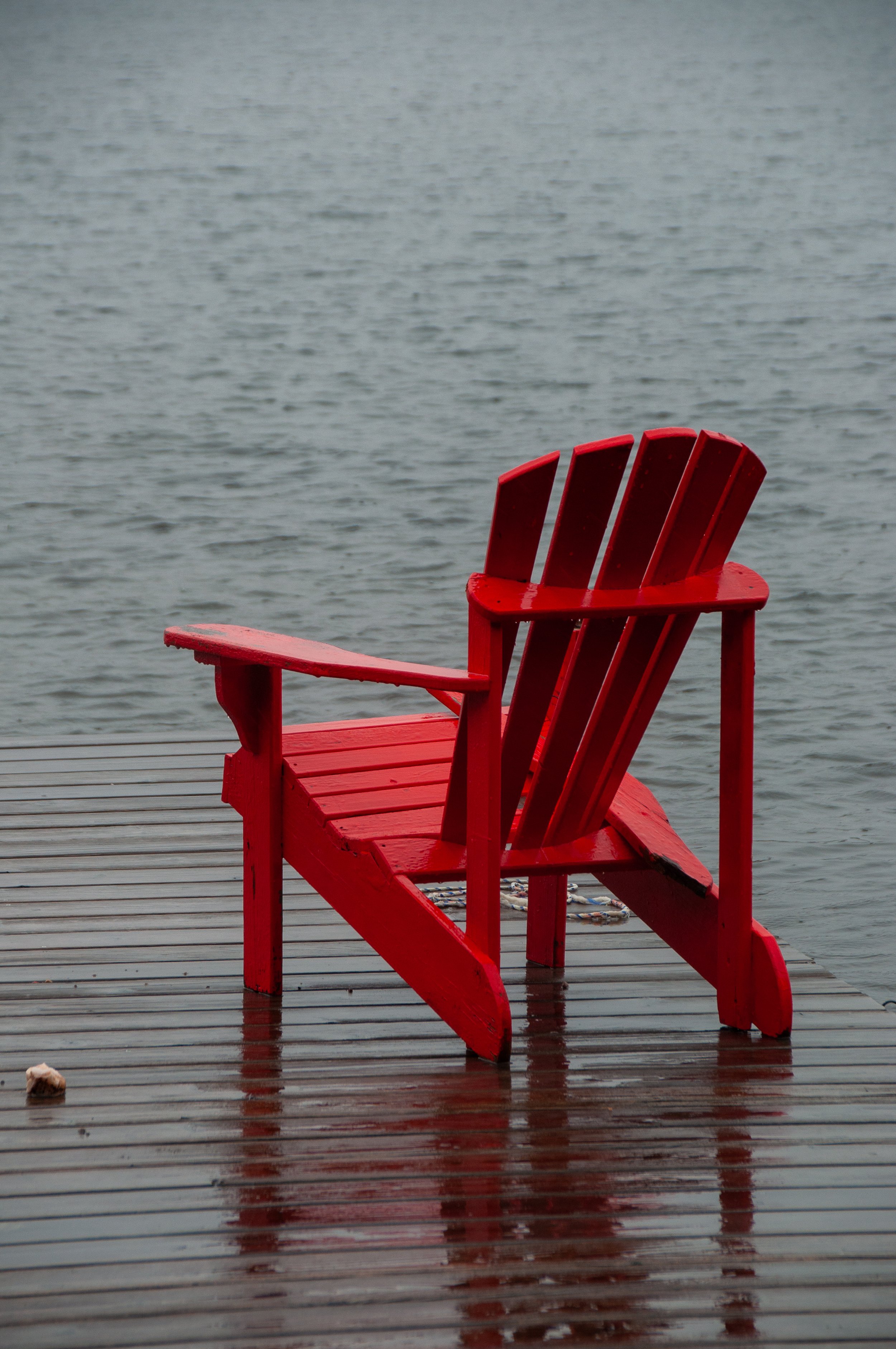 Red Adirondack chair on a wooden dock by a body of water.