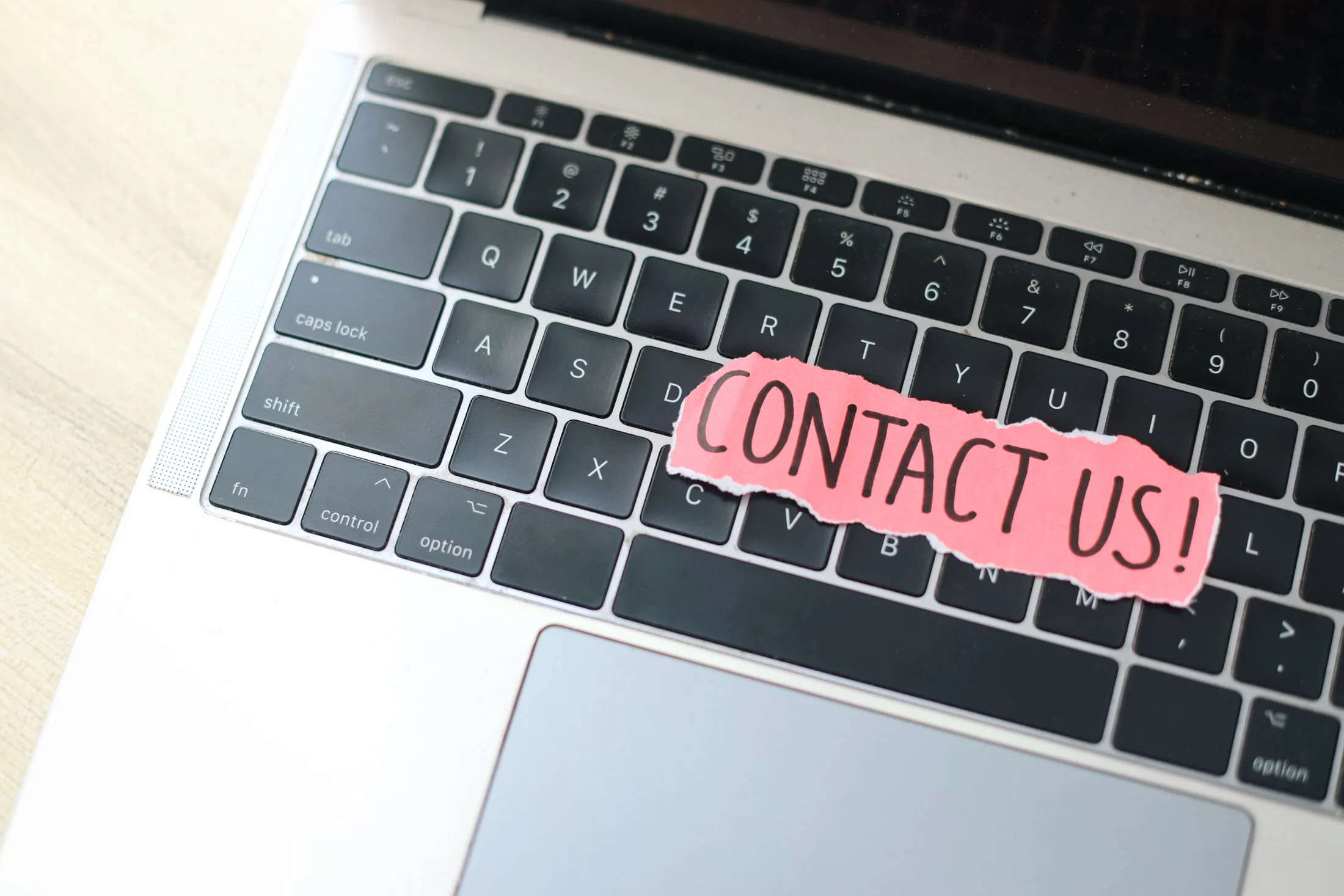 Close-up of a laptop keyboard with a torn pink paper sticker that says 'CONTACT US!'