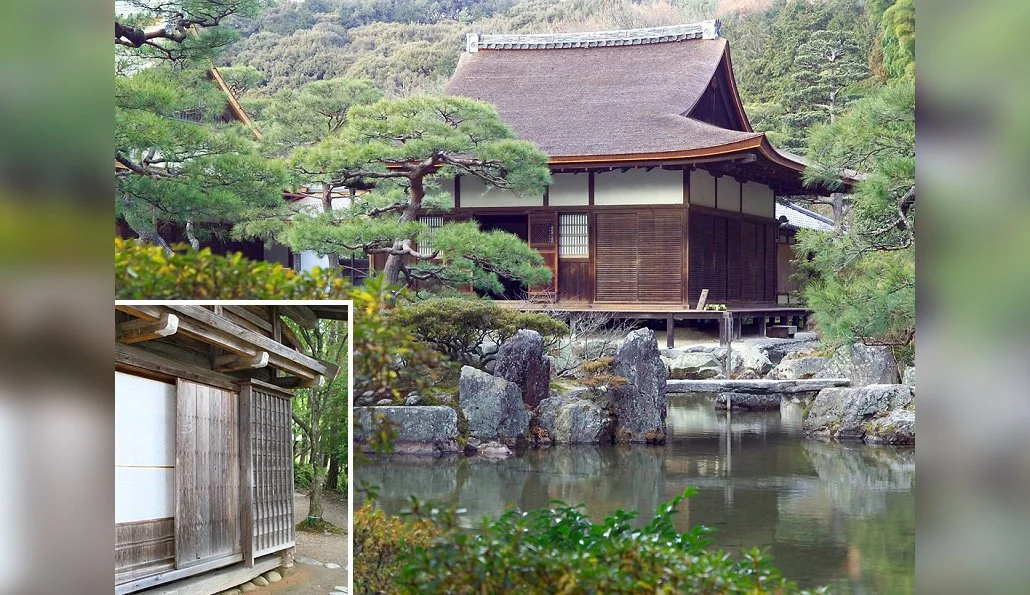 Traditional Japanese house with wooden exterior, surrounded by trees and rocks, reflecting in a pond, with a smaller wooden building in the corner.
