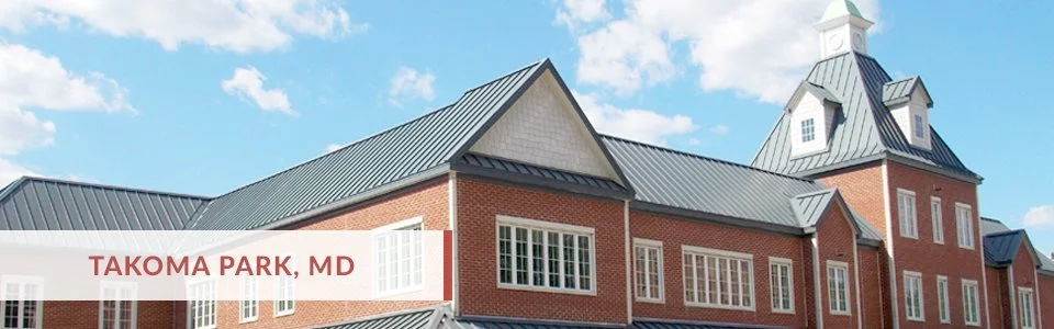 A large brick building with a steep metal roof and a clock tower, under a blue sky with some clouds, with a caption reading 'Takoma Park, MD'.