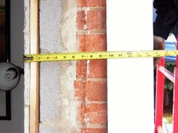 Measuring a brick wall with a yellow tape measure.