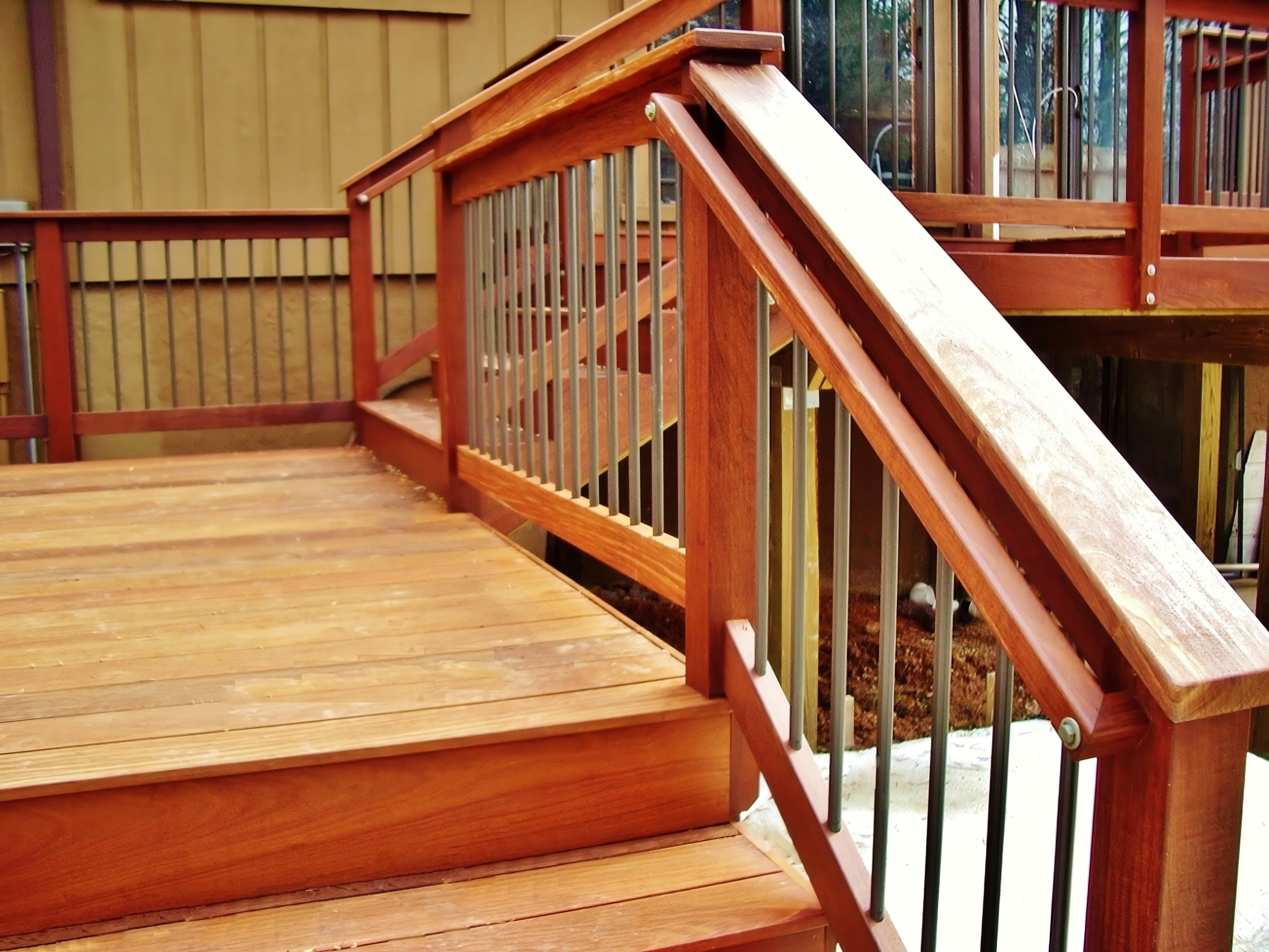 A wooden outdoor deck with railings and stairs leading to a lower level, enclosed by a wooden fenced backyard.