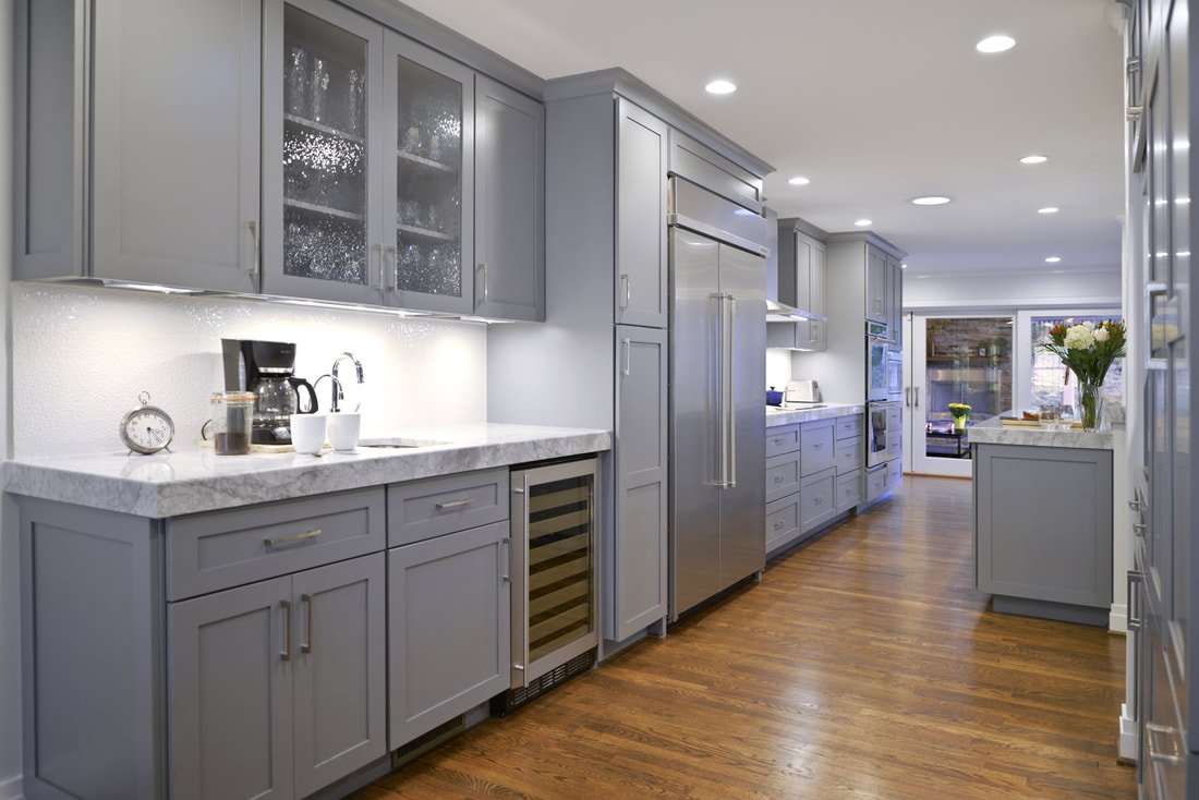 Modern kitchen with gray cabinets, marble countertop, stainless steel appliances, hardwood flooring, and a window with flowers.