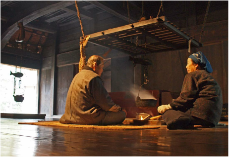 Two women sitting cross-legged on a rug in a traditional kitchen, having a discussion.
