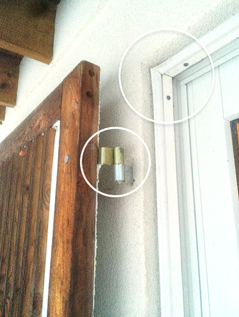 Close-up of a door frame, revealing an exposed screw and a brass door stop mounted on a textured wall.