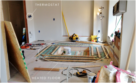 Room under renovation with heating floor installation, construction tools, and an unfinished wall with a thermostat.
