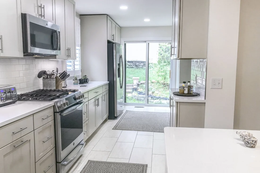 Modern kitchen with white cabinets, stainless steel appliances including a microwave, toaster, and refrigerator, and view of a backyard through sliding glass doors.
