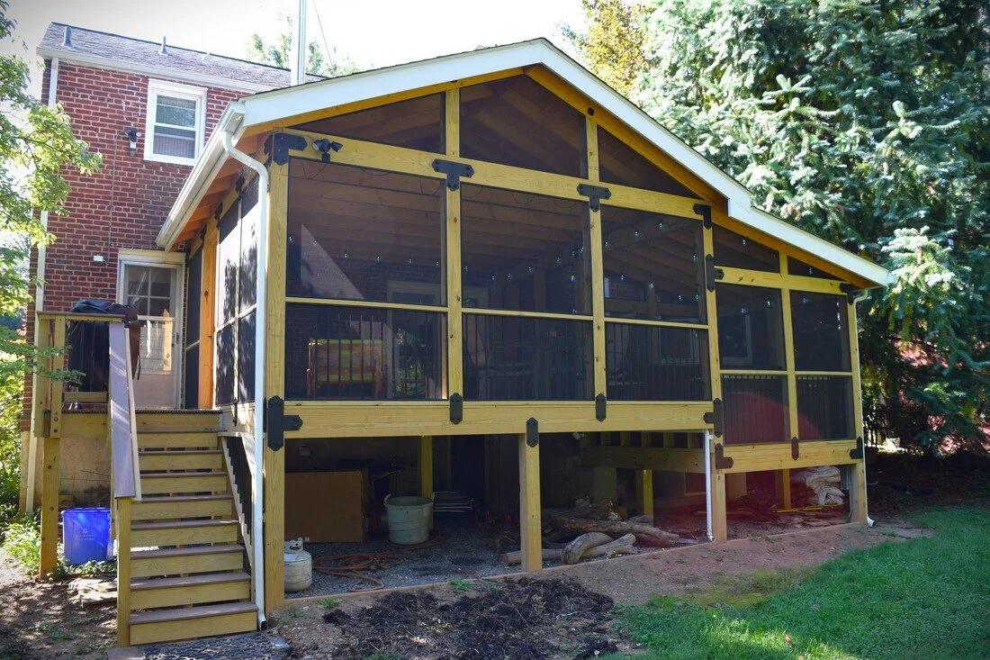 Construction of a screened-in porch or deck attached to a house, with wooden framing and stairs leading up to it.