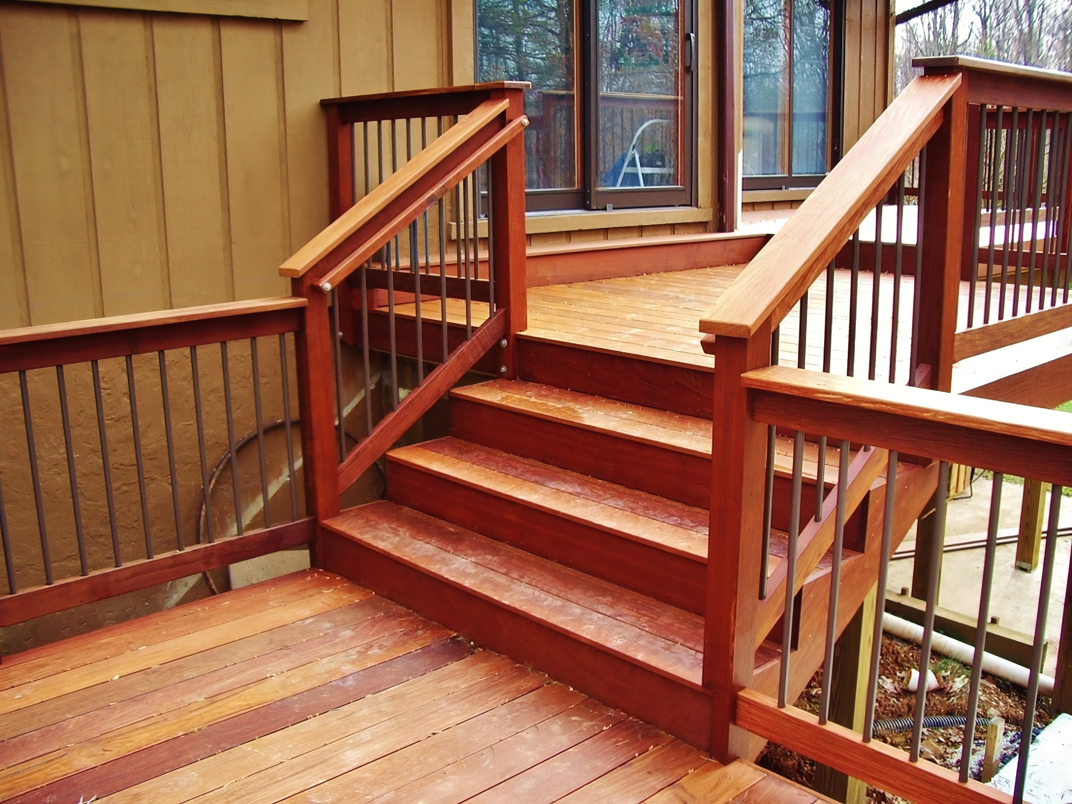 Wooden deck with stairs and railing outside a house with sliding glass doors.