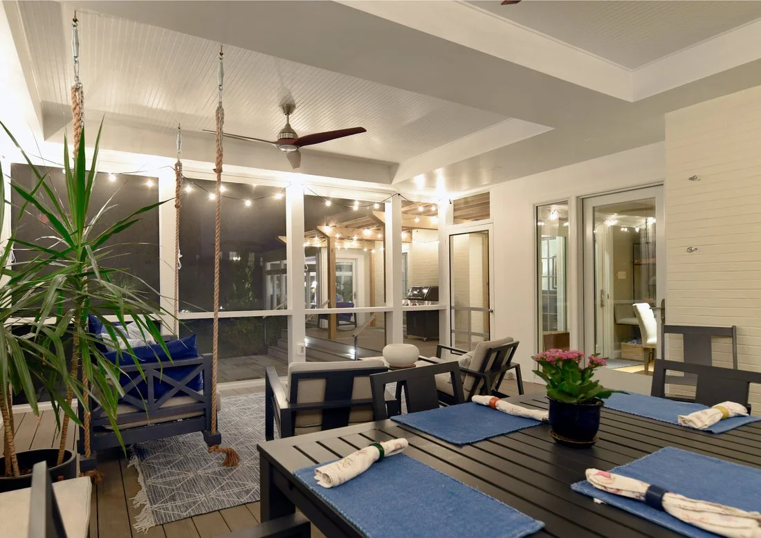 Enclosed porch with dining area, string lights, ceiling fan, potted plant, and outdoor furniture.