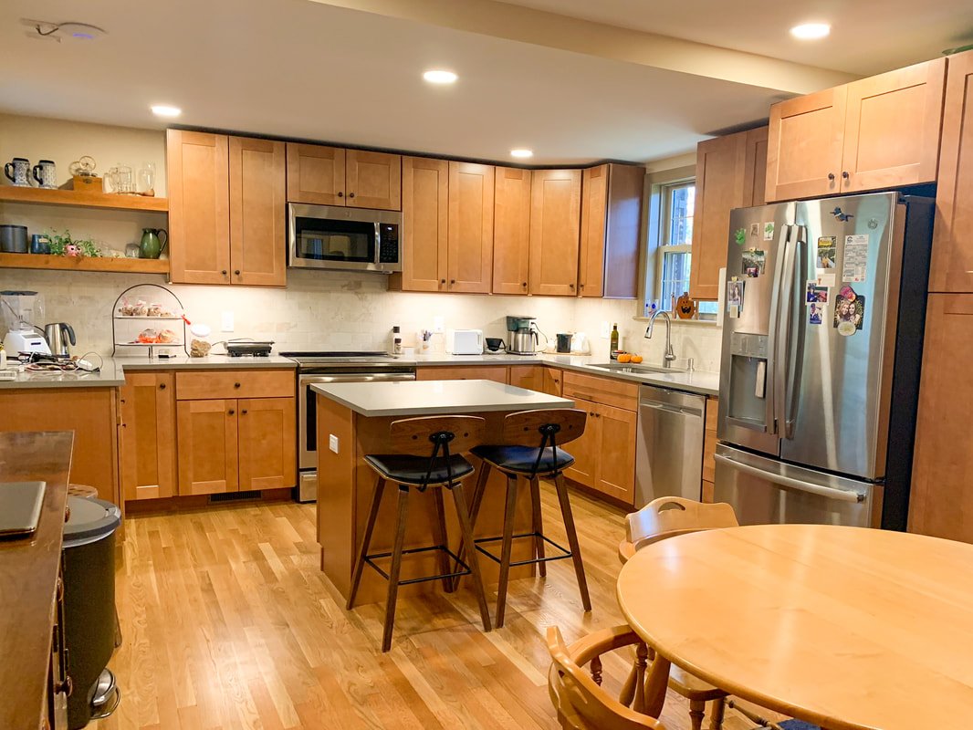 Kitchen with wooden cabinets, stainless steel appliances, a small mobile island with two bar stools, and a round dining table with chairs.