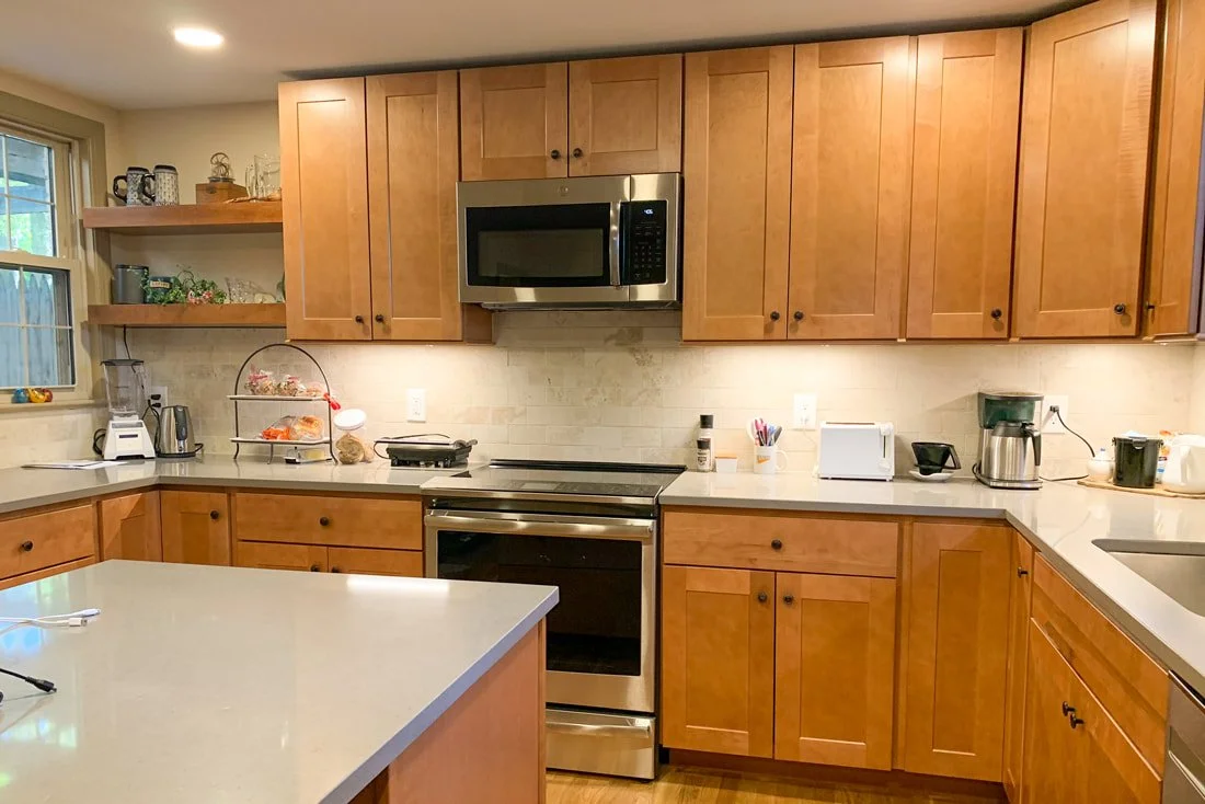 Kitchen with wooden cabinets, microwave oven, stove, toaster, coffee maker, and various kitchen items on counters and shelves.