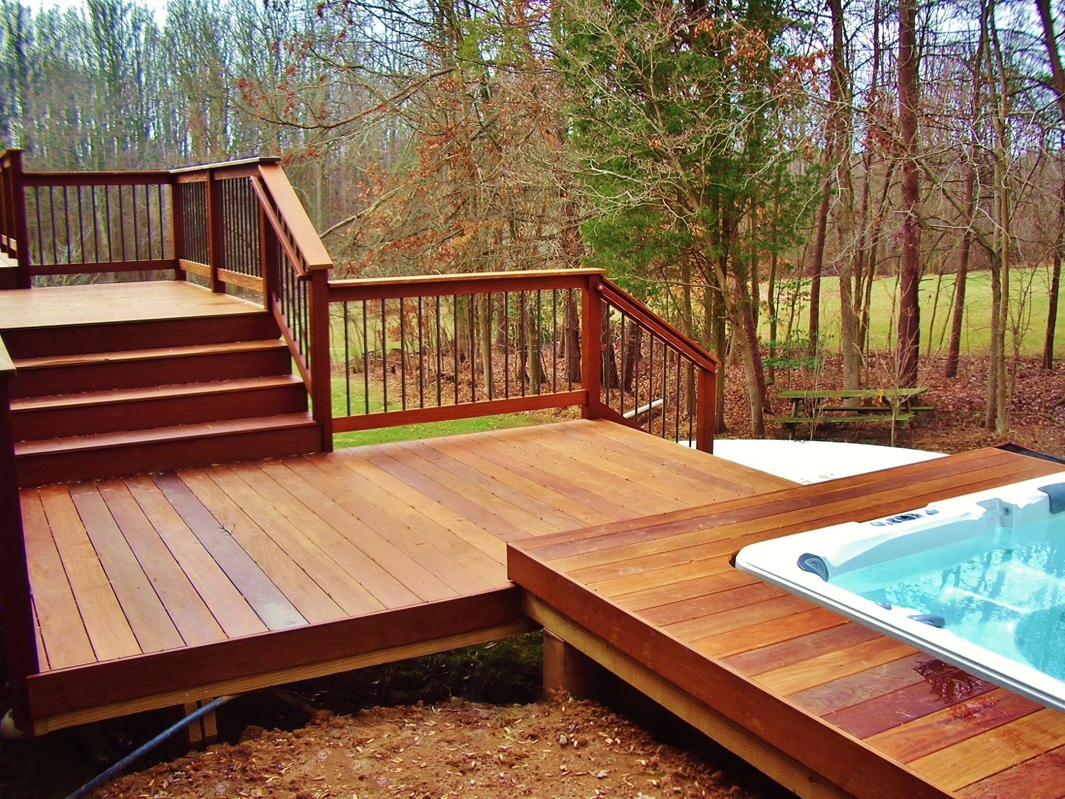 Wooden deck with stairs and a hot tub overlooking a backyard with trees and grass.