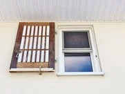 A view of a white house wall with a window and a wooden trellis.