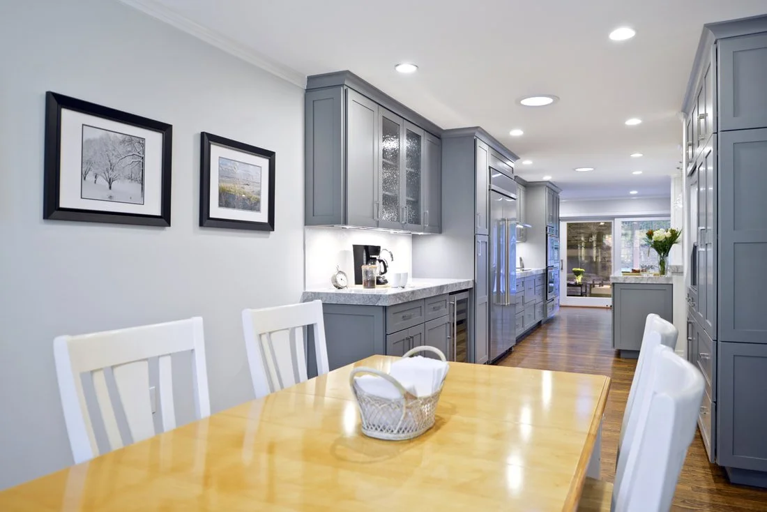 Bright kitchen with gray cabinets, white walls, and a wooden dining table with white chairs.