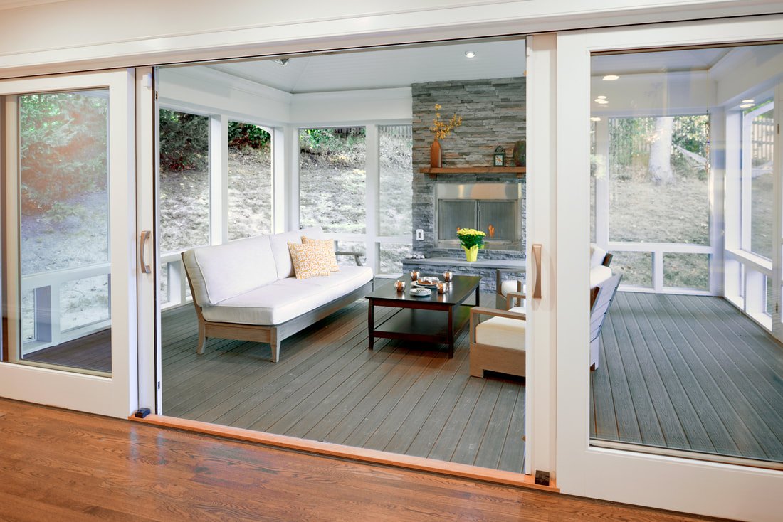 Sunroom with screened glass walls, a white sofa, a fireplace with a stone surround, and chairs around a black coffee table.