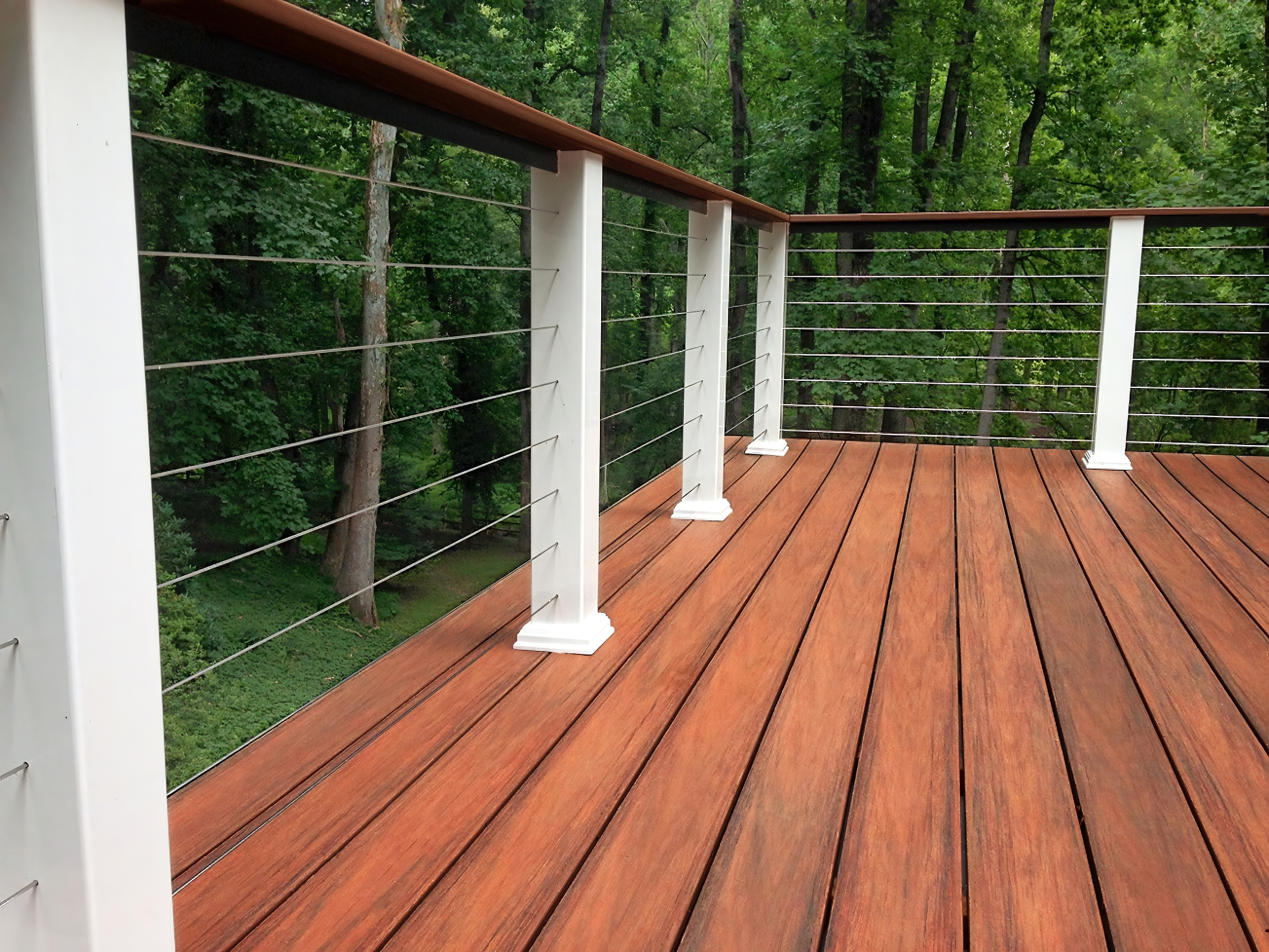 A wooden deck with a white railing overlooking a lush green forest.
