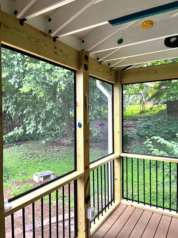 Enclosed porch with wooden framing, screen walls, and a dirt yard with trees outside.