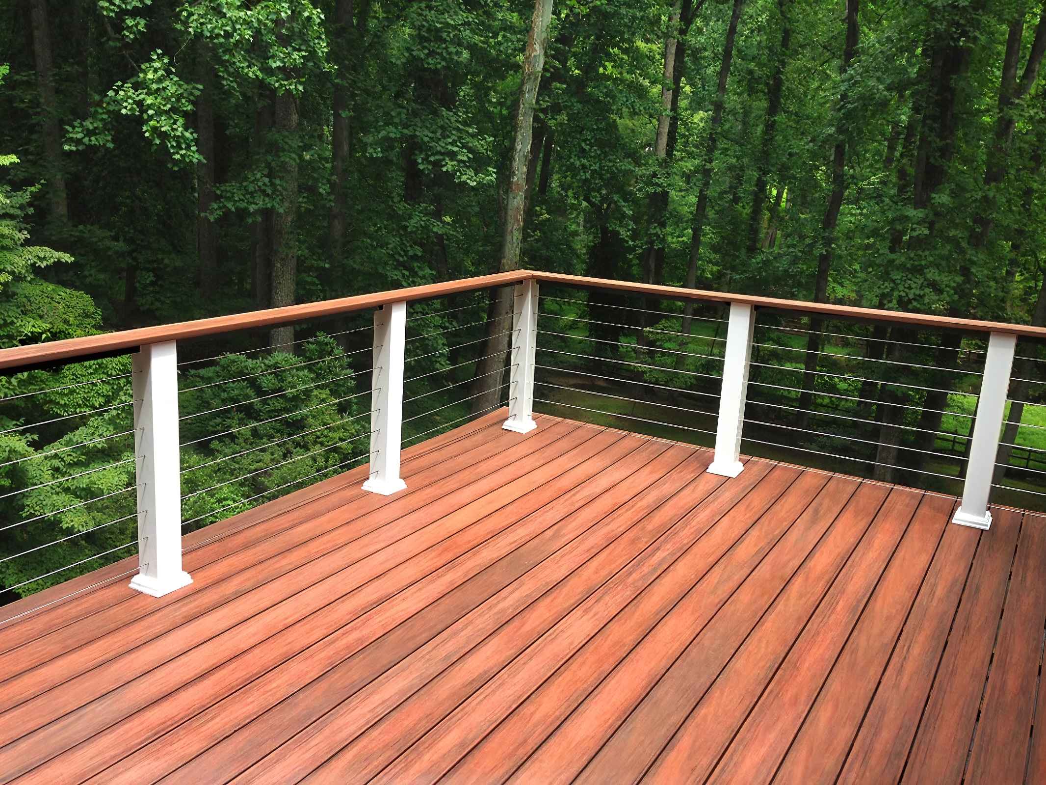 Wooden deck with metal and wooden railing overlooking a forest with tall green trees.