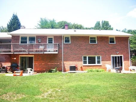 Back of a brick house with a grassy yard, a second-story balcony, and sliding glass doors on the ground level.