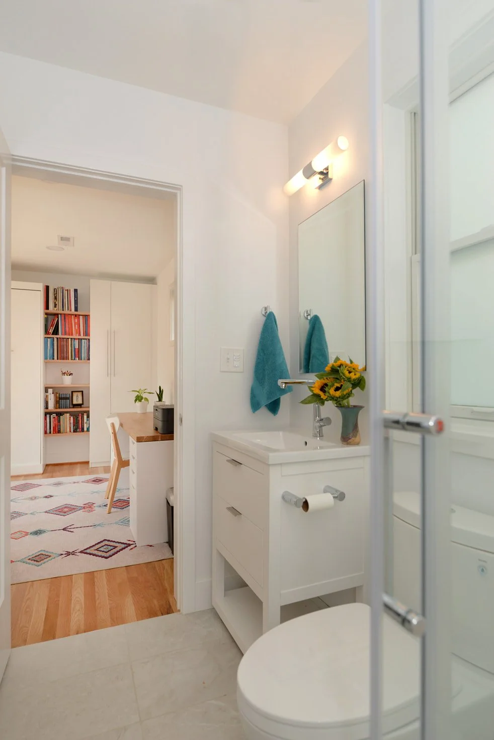 Bathroom with white vanity, mirror, blue towels, sunflower bouquet, and shower glass door