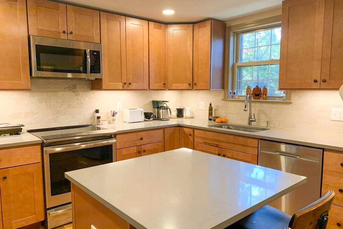 Kitchen with wooden cabinets, white countertop, stainless steel microwave, oven, and dishwasher, window with halloween decorations, and an orange pumpkin.