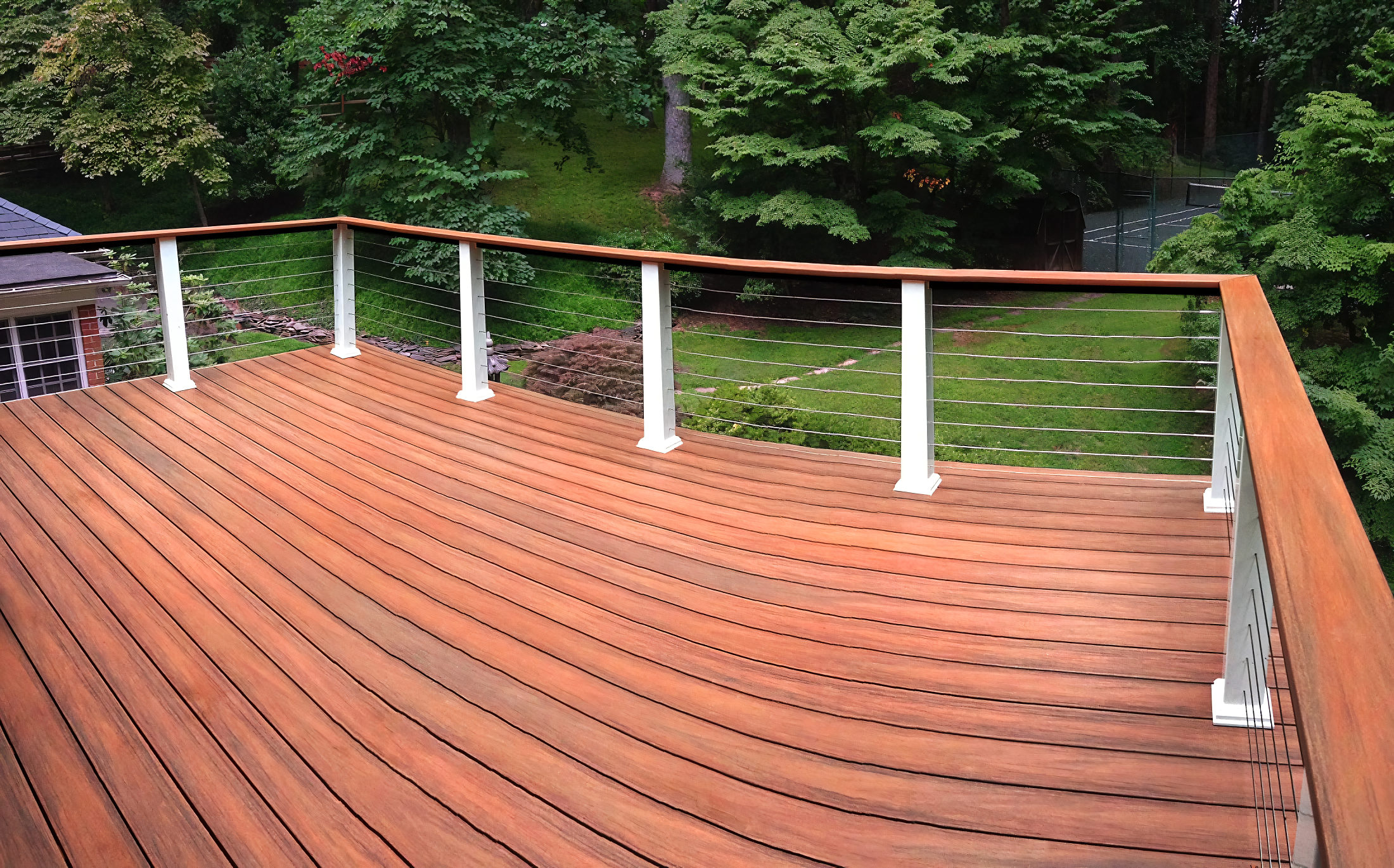 Wooden deck with metal railing overlooking a lush green backyard with trees and grass.