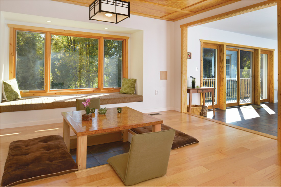 Living room with large front window, wooden accents, a seating nook with pillows, and a dining area with sliding glass doors leading outside.