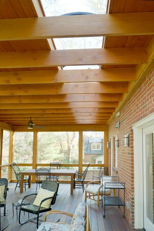 Enclosed porch with wooden ceiling beams, brick wall, and patio furniture including chairs, a table, and a small side table.