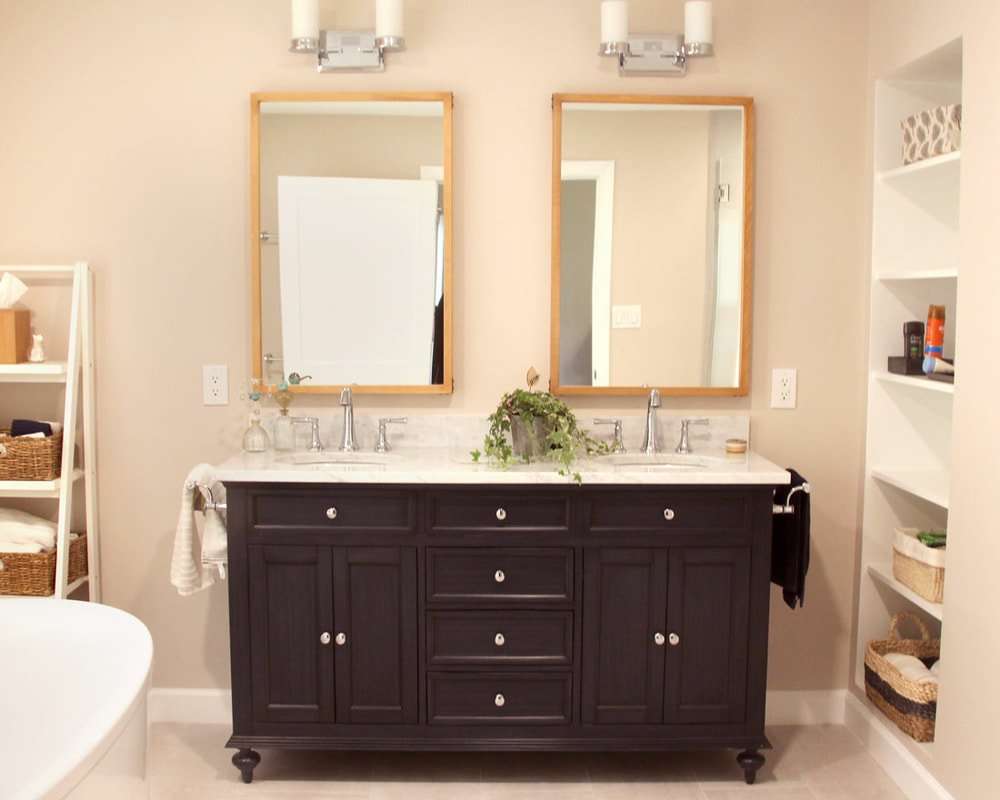 Bathroom vanity with two mirrors, a double sink, and dark wood cabinetry. There are shelves with baskets on the sides, and a plant placed on the counter.