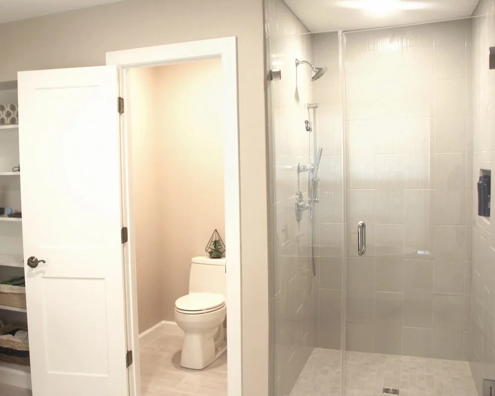 View of a modern bathroom with a glass-enclosed shower and a separate toilet area, featuring beige wall tiles and white fixtures.