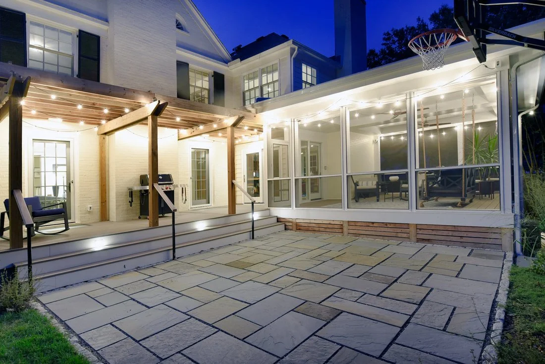 Backyard with patio, string lights, and a screened porch, part of a large house with windows and a basketball hoop