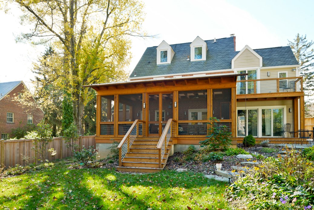 Rear view of a house with a newly built screened-in porch and deck, surrounded by trees and a landscaped yard.